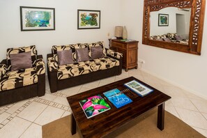 A living room with two patterned sofas, a coffee table with magazines, and a large mirror. - Melaleuca Resort (Palm Cove)