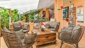 Un espacio al aire libre acogedor con mobiliario de mimbre, una mesa de centro de madera y diversas plantas en macetas.
