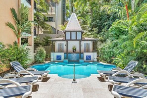A pool area with lounge chairs and a small building with a tiled roof. - Martinique on Macrossan (Port Douglas)