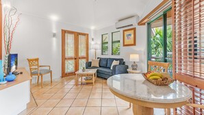 Amplia sala de estar con sofá, mesa de centro y mesa de comedor con una cesta de frutas.
