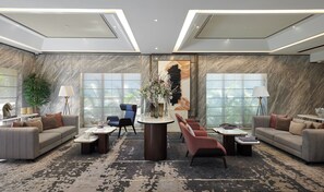 A modern lobby with a marble wall, a central table with vases, sofas, and a large window with a view of palm trees. - Astoria Hotel (Mumbai)