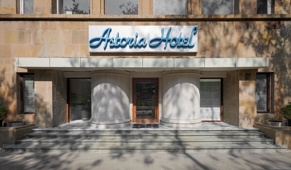 The exterior of the Astoria Hotel with a prominent sign, a set of steps leading to the entrance, and two large columns framing the door. - Astoria Hotel (Mumbai)