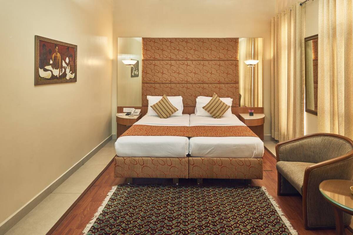 A hotel room with a double bed, two nightstands, a chair, a small table, and a patterned rug.