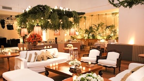 Un salon bien éclairé et élégamment aménagé, avec des canapés blancs, des fauteuils et une table basse décorée de fleurs et de bougies.
