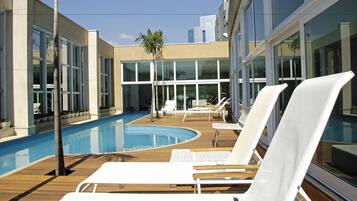 Relax by the pool surrounded by comfortable lounge chairs and a lush palm tree.