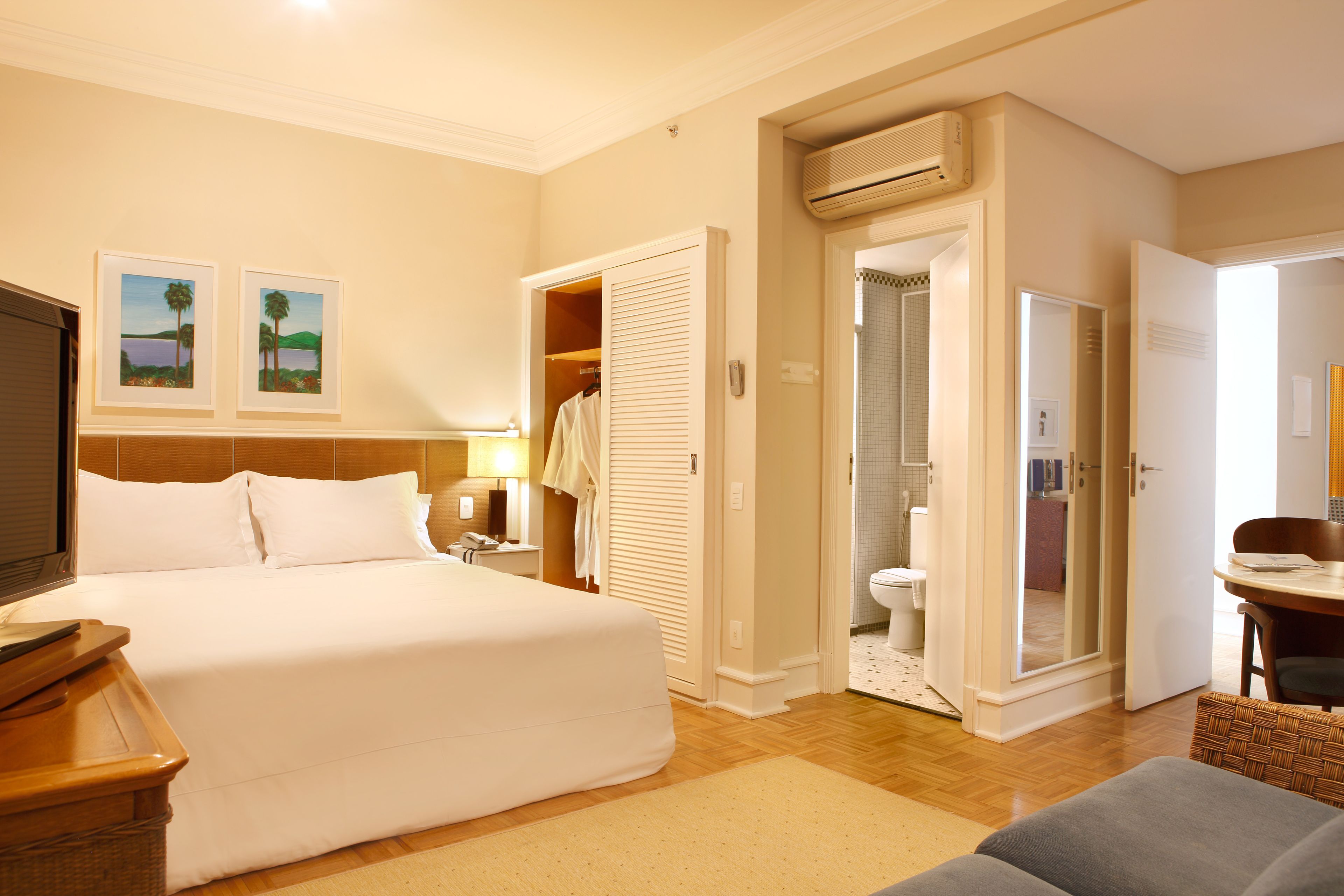 A hotel room with a large bed, a desk with a chair, a wardrobe, and an air conditioning unit.