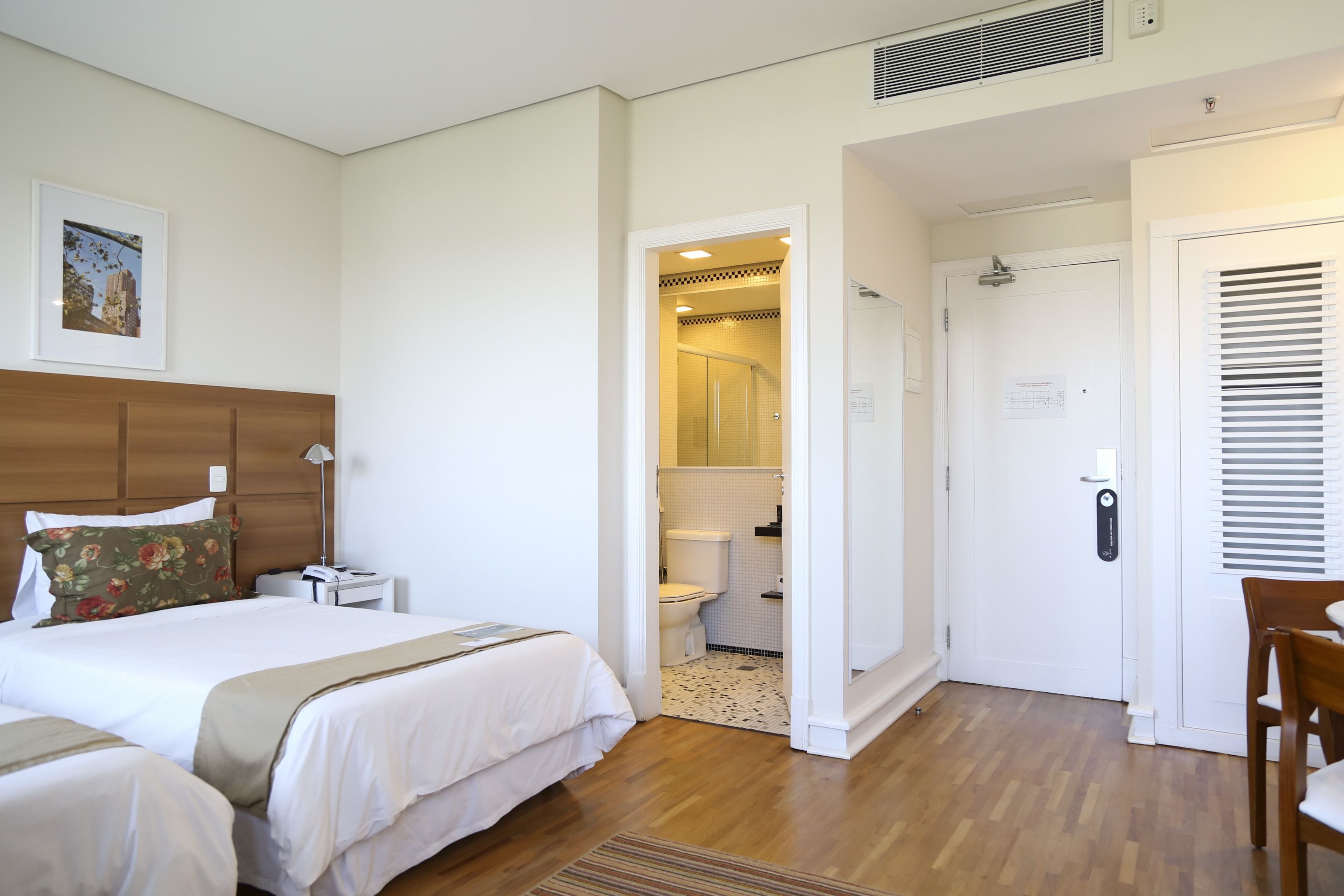A hotel room with a large bed, a bedside table, a chair, and a bathroom visible through an open door.