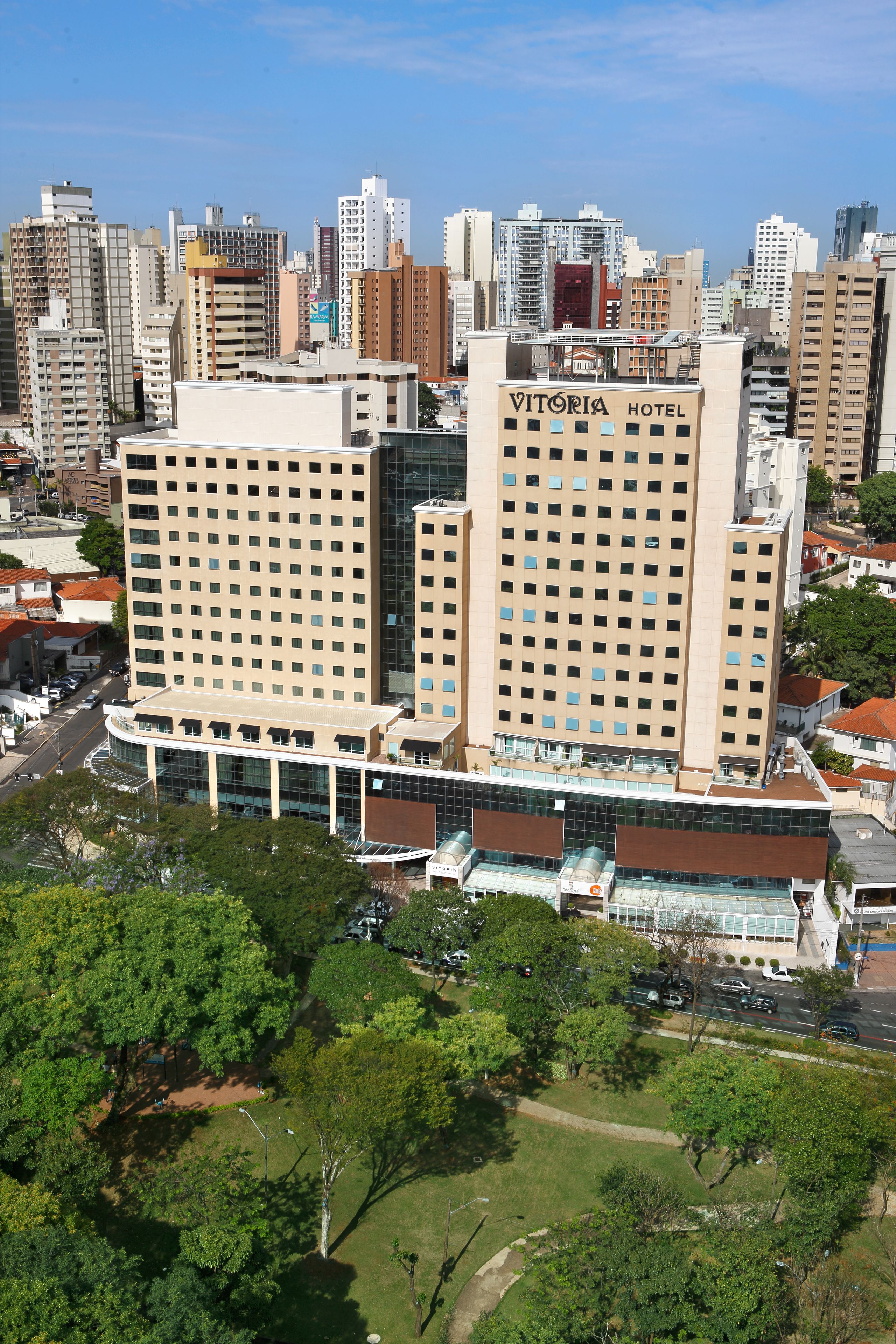 A hotel with a modern design, featuring a prominent 'Vitoria Hotel' sign, surrounded by a dense urban environment with high-rise buildings.