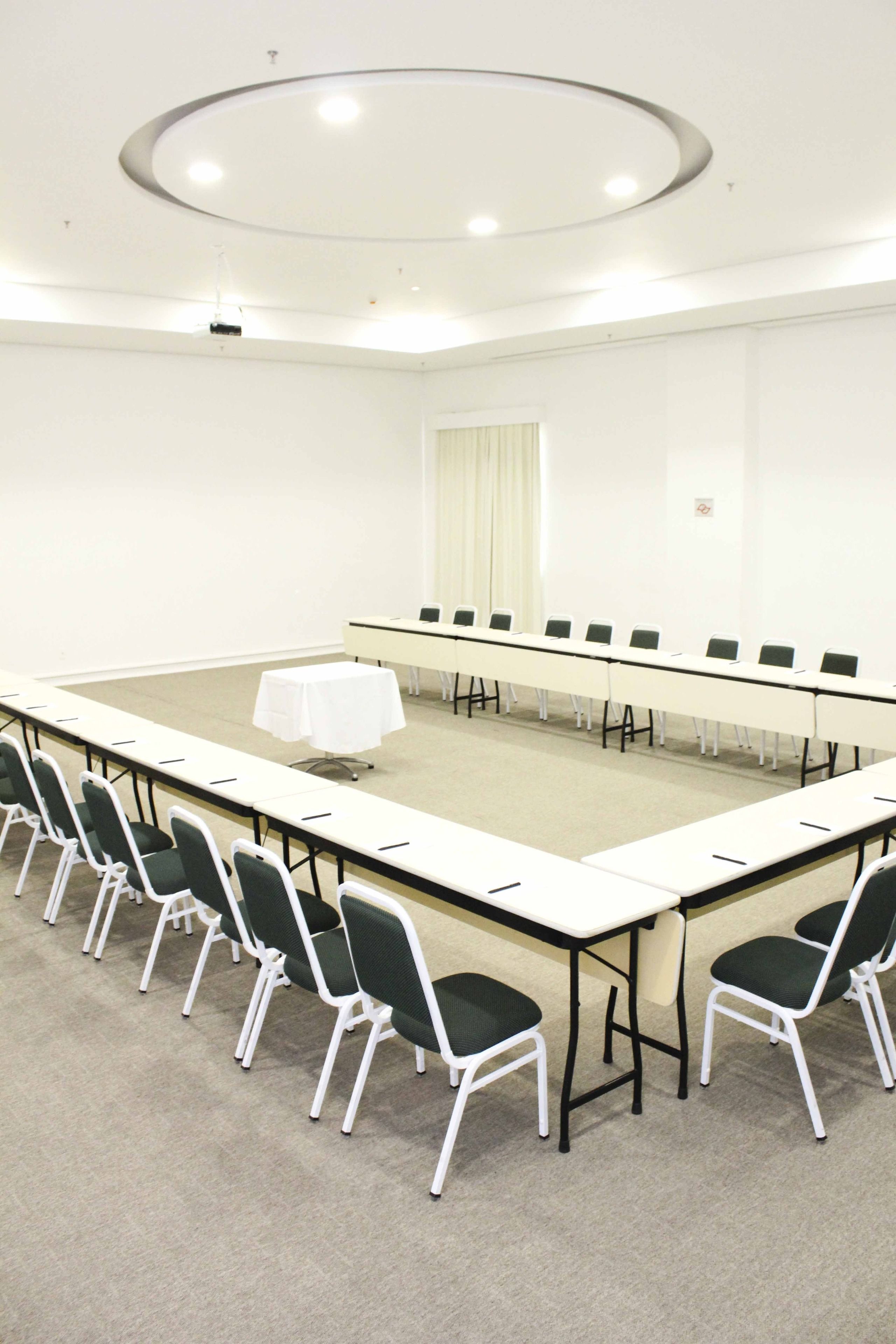 Sala de conferências com uma mesa comprida, cadeiras, um projetor e toalha de mesa branca.