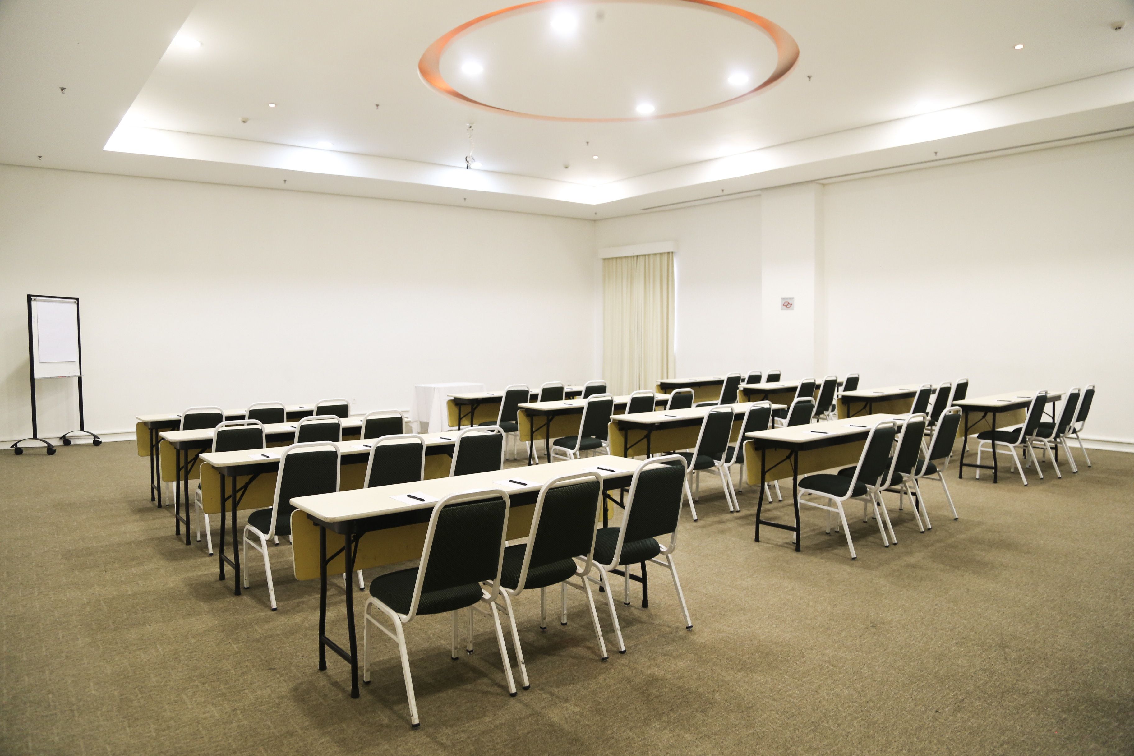 A conference room with rows of tables and chairs, a whiteboard, and a projector screen.