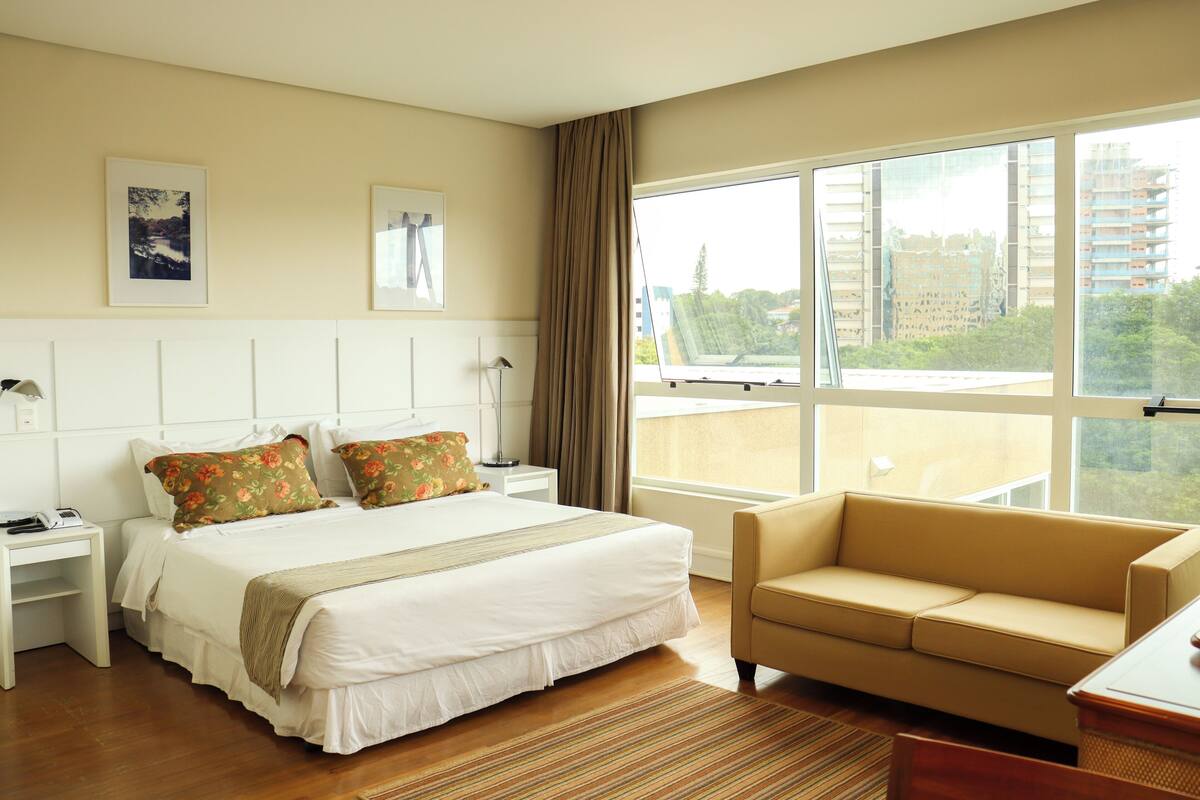 Een hotelkamer met een groot bed, een bank, een bureau en een raam met uitzicht op de stad.