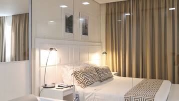 A modern hotel room with a large bed, a separate bathroom with a bathtub, a bedside table with a lamp, and a large mirror.