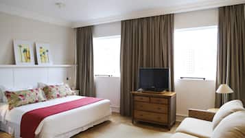 A hotel room with a bed, a television, a dresser, a sofa, and two windows with curtains.