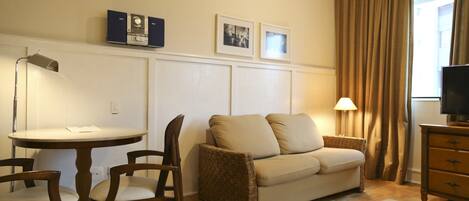 A hotel room with a round dining table, two chairs, a sofa, a TV stand, and a lamp.