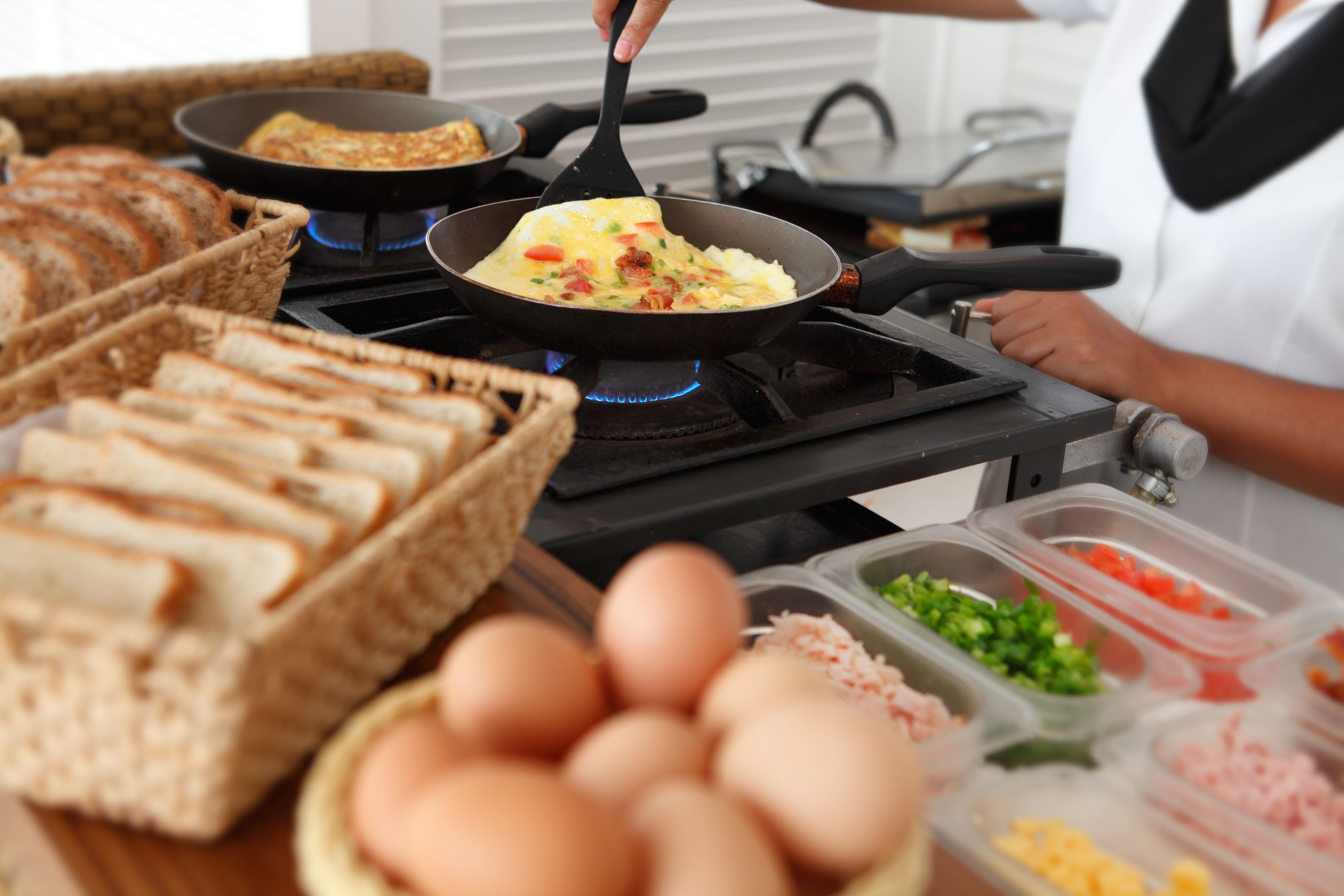 A kitchen with a frying pan on a stove, a basket of bread, and containers of ingredients.