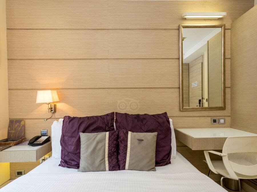 Una habitación de hotel con una cama, un escritorio con lámpara, una silla y un espejo grande.