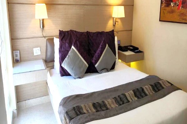 Habitación de hotel con cama, dos lámparas de noche, mesita con teléfono y un cuadro en la pared.
