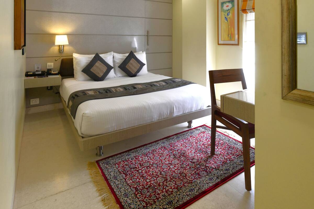 A hotel room with a bed, bedside table, lamp, and a chair.