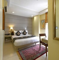 A hotel room with a bed, bedside table, lamp, and a chair.