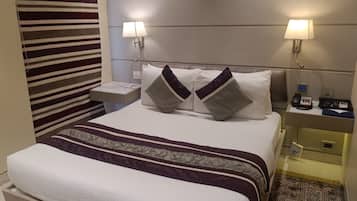 Habitación de hotel con una cama bien hecha, dos lámparas de noche, una mesita de noche con un teléfono y una pequeña mesa, y una cortina a rayas.