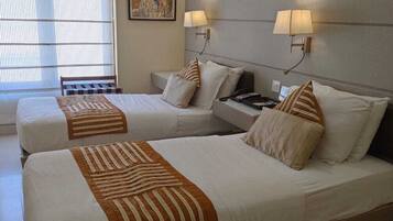A hotel room with two beds, each with a striped bedspread, a bedside table with a lamp, and a window with blinds.