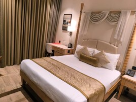 A hotel room with a large bed, a desk, a chair, a bedside table, and a lamp.