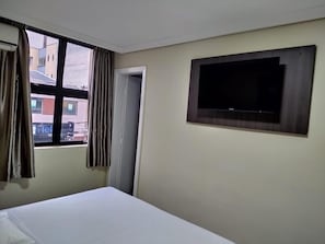 A hotel room with a bed, a window with curtains, a door, and a mounted TV. - Hotel Estação Express (Curitiba)