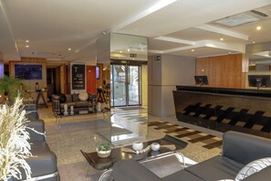 A hotel lobby with a reception desk, seating area, and a large mirror. - SLAVIERO Curitiba Batel (Curitiba)