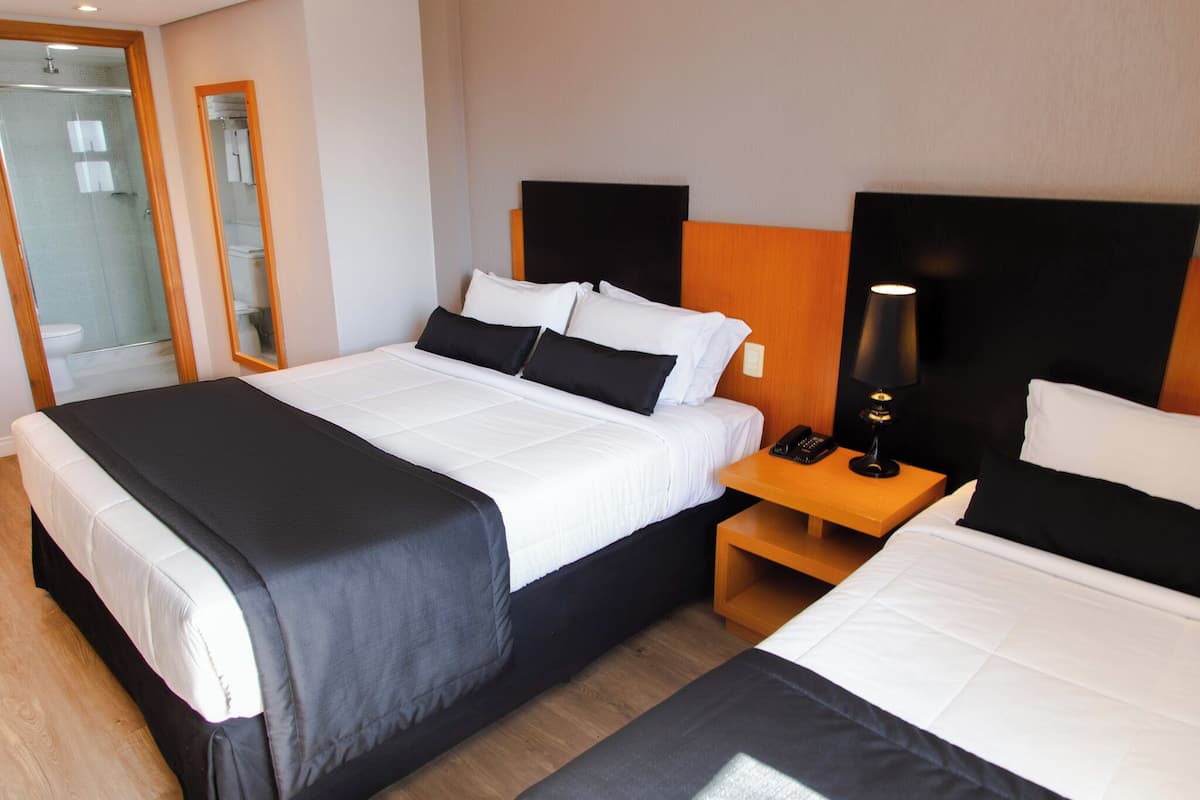 Una habitación de hotel con una cama grande, una mesita de noche con lámpara y un espejo.