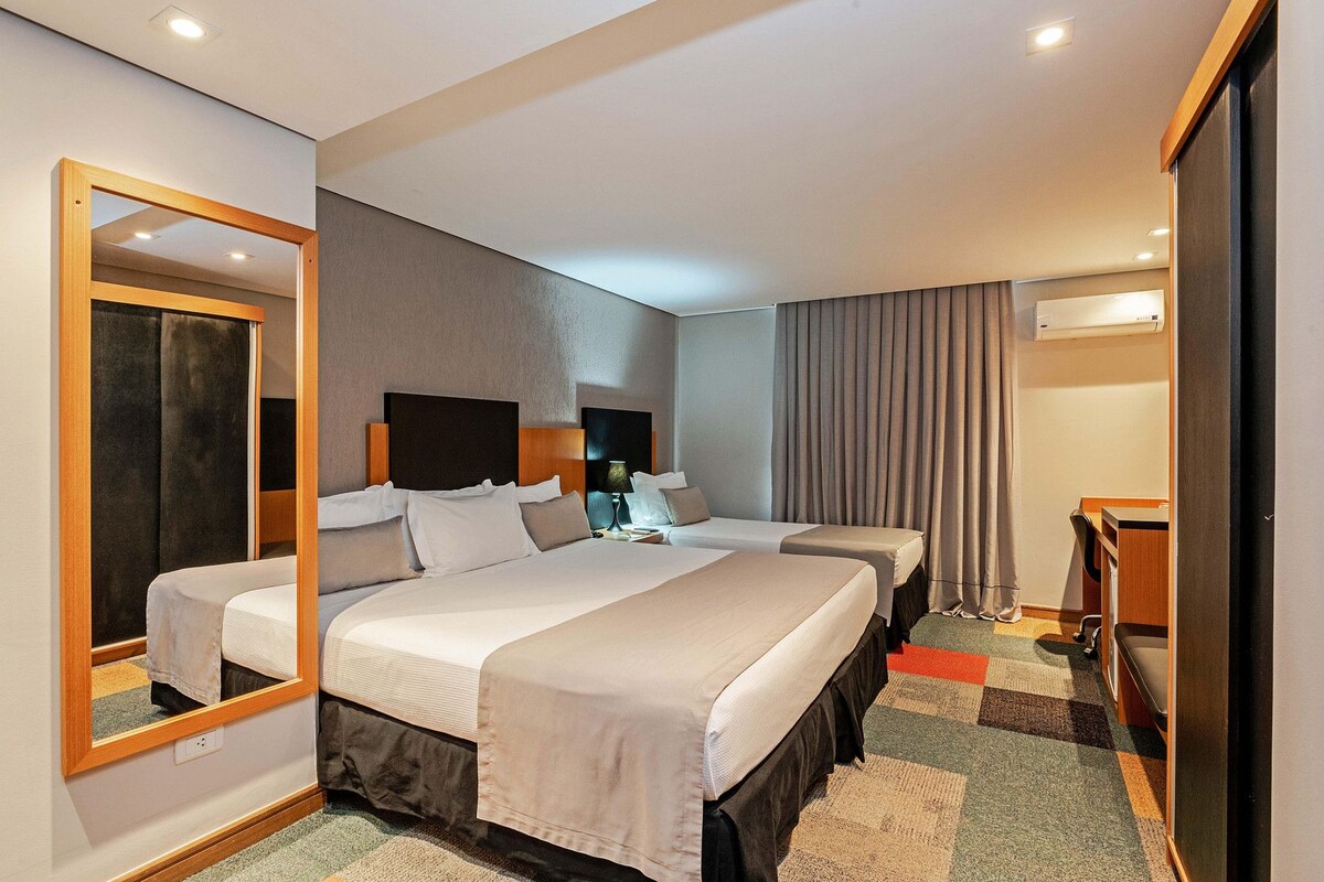 A hotel room with two beds, a large mirror, a desk, and a chair.