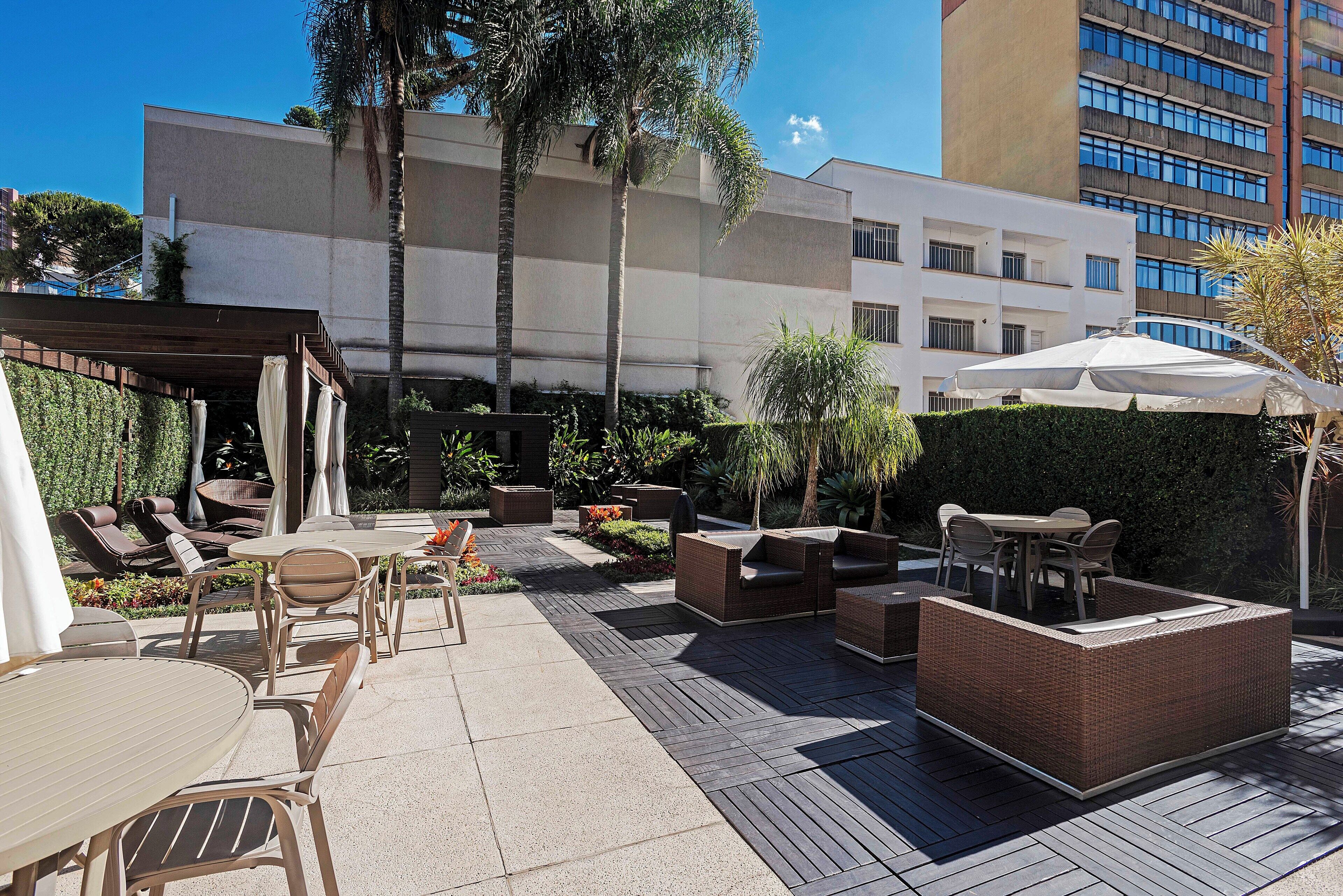 An outdoor patio area with seating arrangements, a covered table, and a view of a modern building in the background.