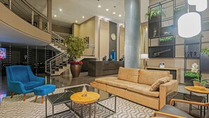 Un vestíbulo amplio con un diseño moderno, que incluye un sillón azul, un sofá color crema y una escalera que lleva a un nivel superior.