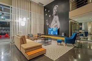 Un moderno hall de hotel con un gran mural en la pared, una zona de estar con sofás y sillones, y un puerta de vidrio que da al exterior.