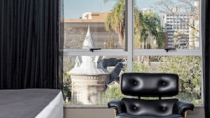 Una habitación de hotel moderna con un ventanal grande, un sillón de cuero negro y una cama.