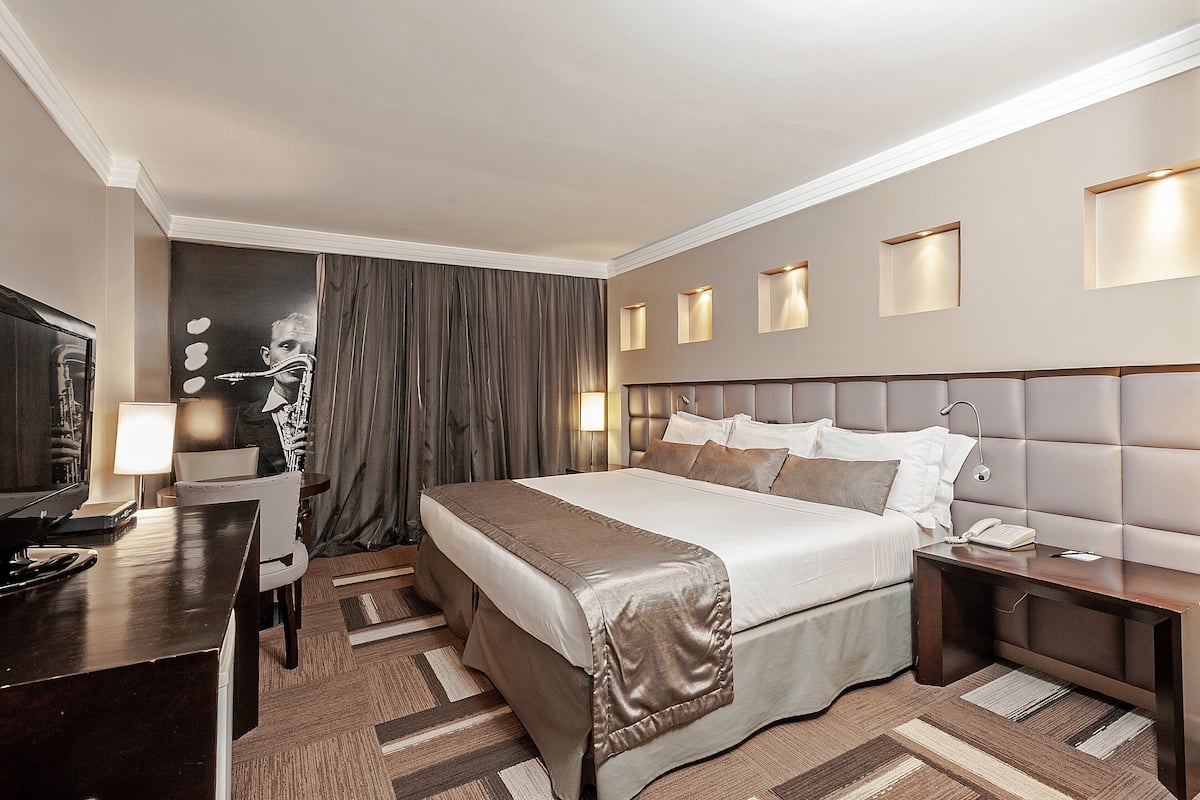 Una habitación de hotel con una cama grande, mesitas de noche, un escritorio con lámpara y una televisión.