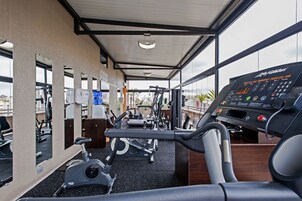 Un gimnasio con equipo de ejercicio, un panel de control y grandes ventanales con vistas a la ciudad.