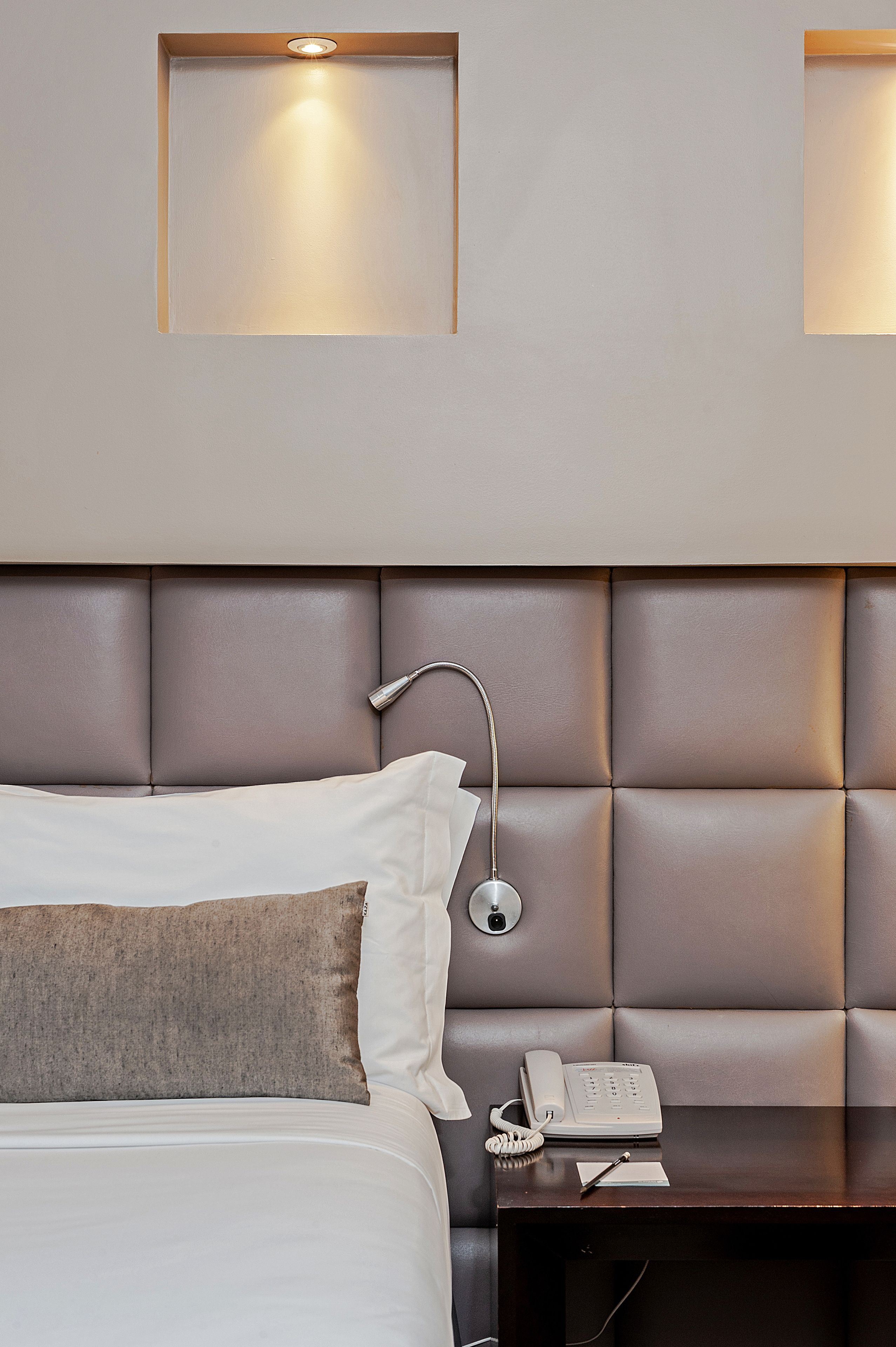 A hotel room with a bed, a bedside table with a telephone, and a wall-mounted light fixture.