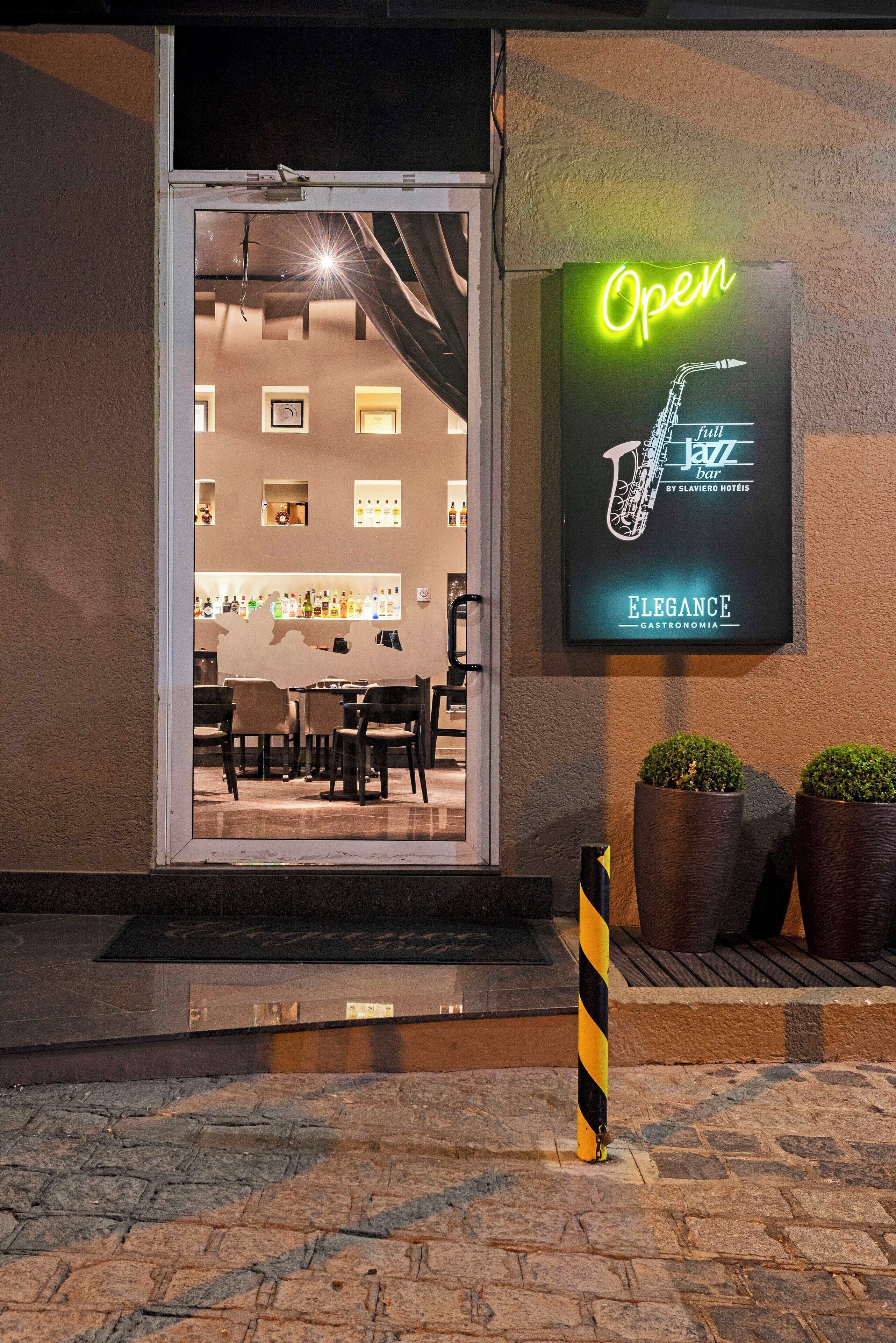 L’entrée d’un restaurant, avec une enseigne néon indiquant « Ouvert », un motif représentant un saxophone et une autre enseigne indiquant « Bar de jazz ».