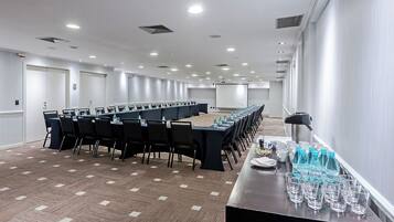 Un salón de conferencias con una larga mesa, sillas, una pantalla de proyector y botellas de agua.