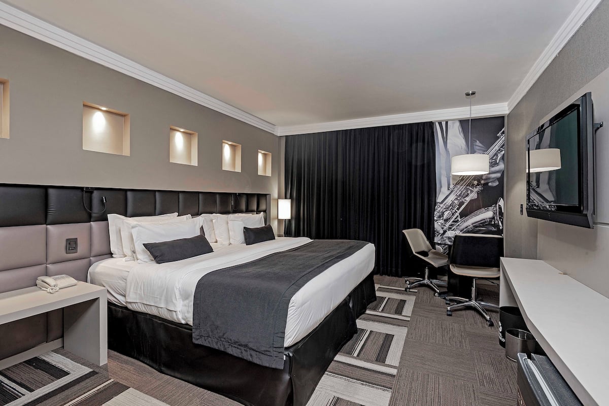 Una habitación de hotel moderna con una cama grande, mesitas de noche, un escritorio y un televisor.
