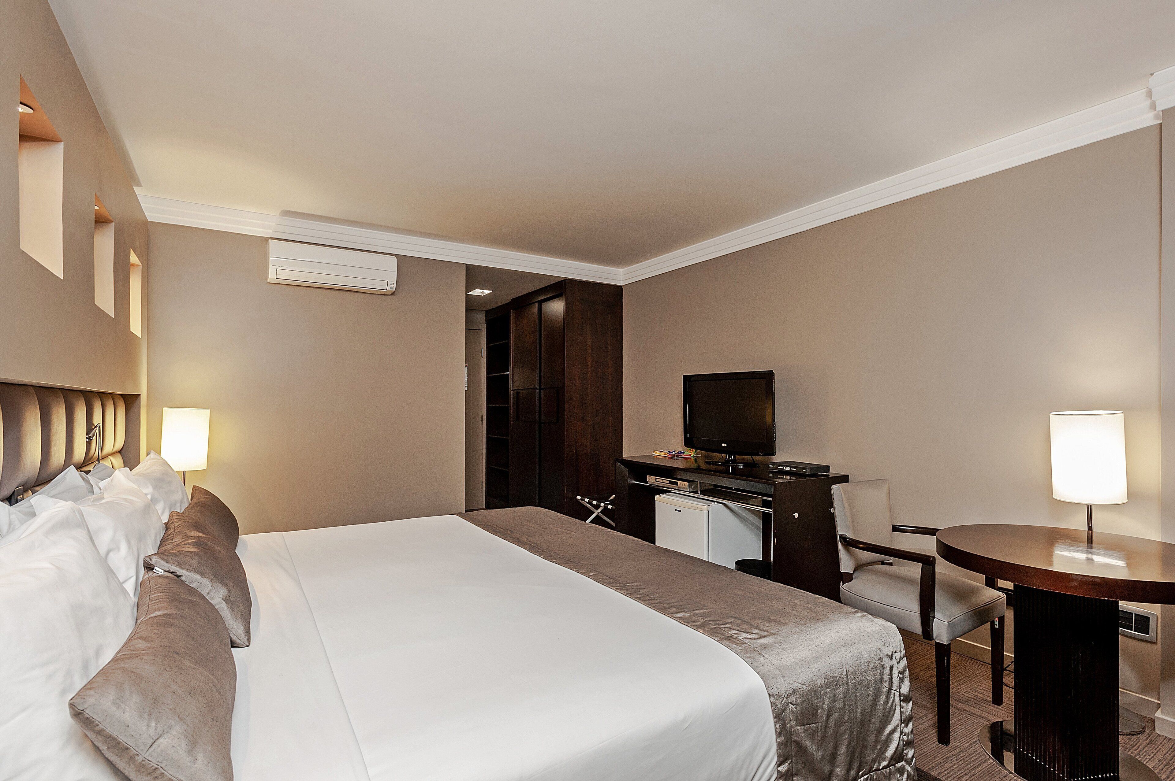 A hotel room with a large bed, a desk, a chair, a television, and a lamp.