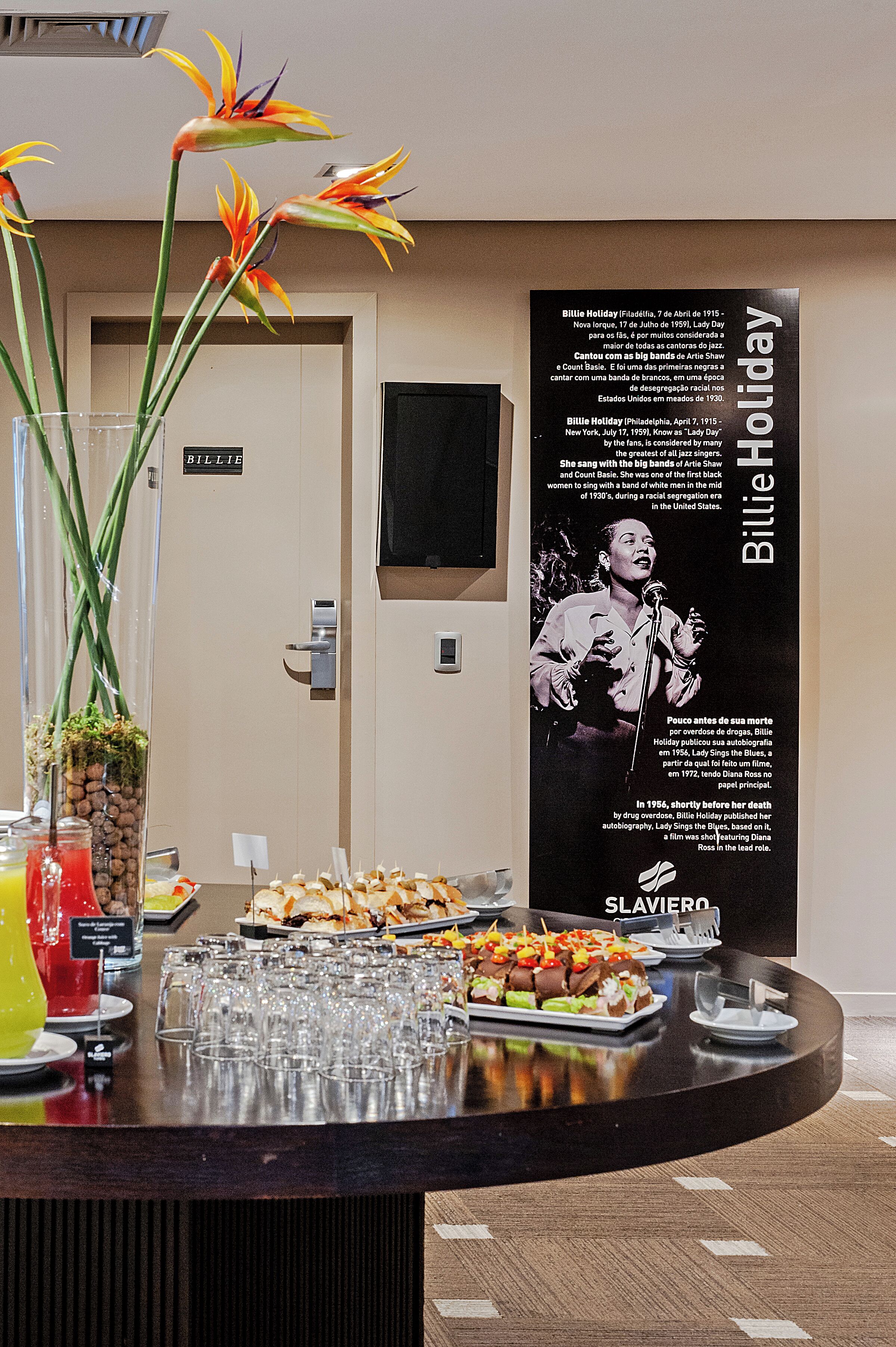 A buffet table with food and drinks, a poster of Billie Holiday, and a door labeled "BILLIE".
