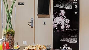 A buffet table with food and drinks, a poster of Billie Holiday, and a door labeled "BILLIE".