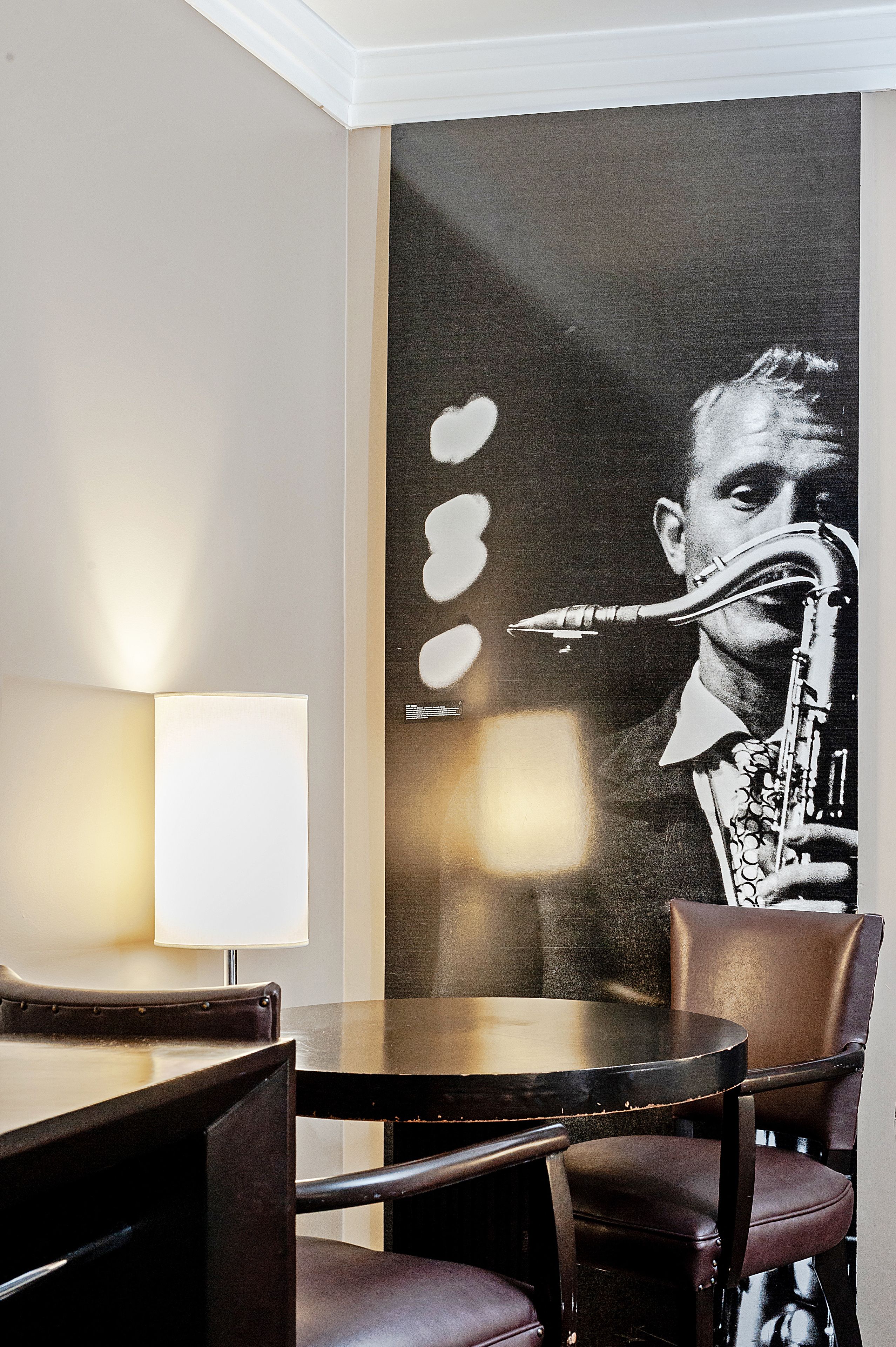 A dining area with a table and chairs, a lamp, and a large wall mural of a saxophonist.