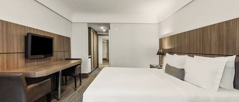 A hotel room with a bed, a desk, a chair, a television, and a lamp.