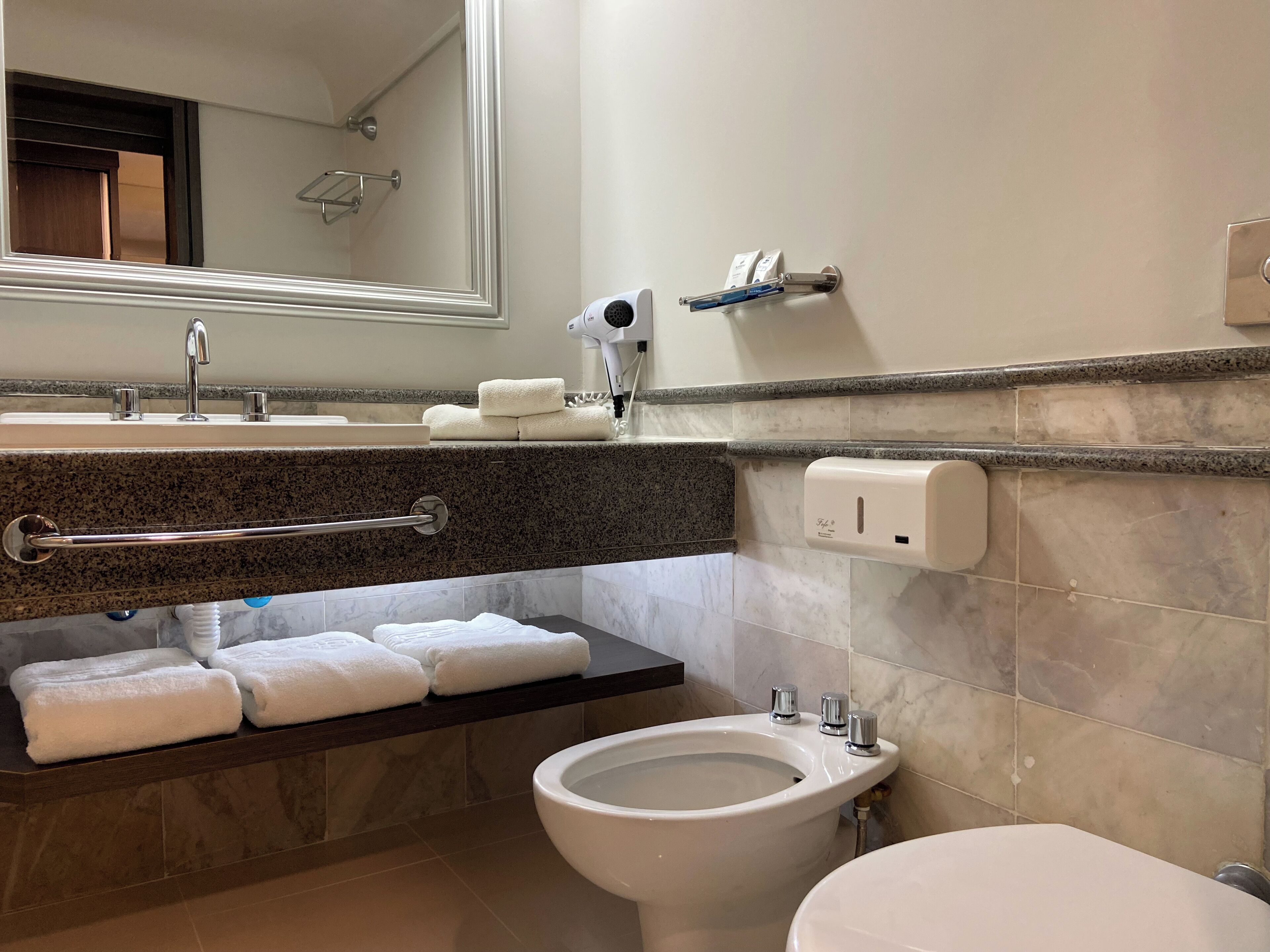 Ein modernes Badezimmer mit einer Granitplatte, einem integrierten Handtuchhalter, einem Bidet und einem Händetrockner.