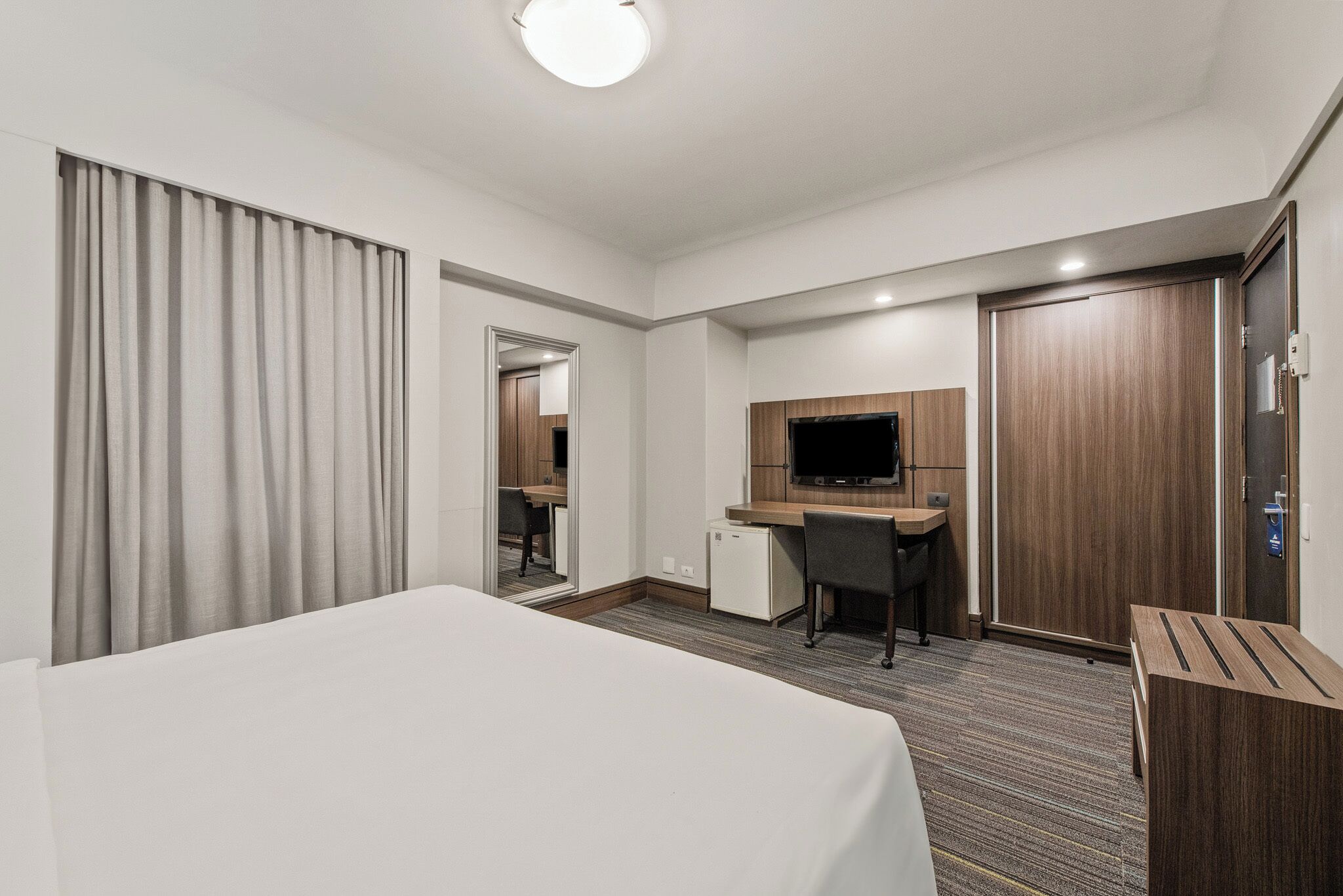 Una habitación de hotel con una cama, un escritorio con una computadora, una televisión y un armario.