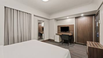 Una habitación de hotel con una cama, un escritorio con una computadora, una televisión y un armario.