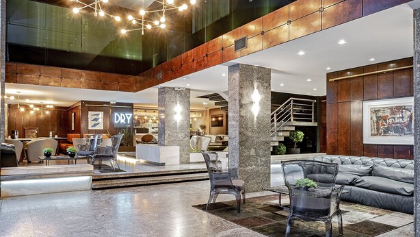 A spacious lobby with a modern design, featuring a seating area with leather sofas and chairs, a reception desk, and a staircase leading to upper floors. - SLAVIERO Curitiba Centro  (Curitiba)