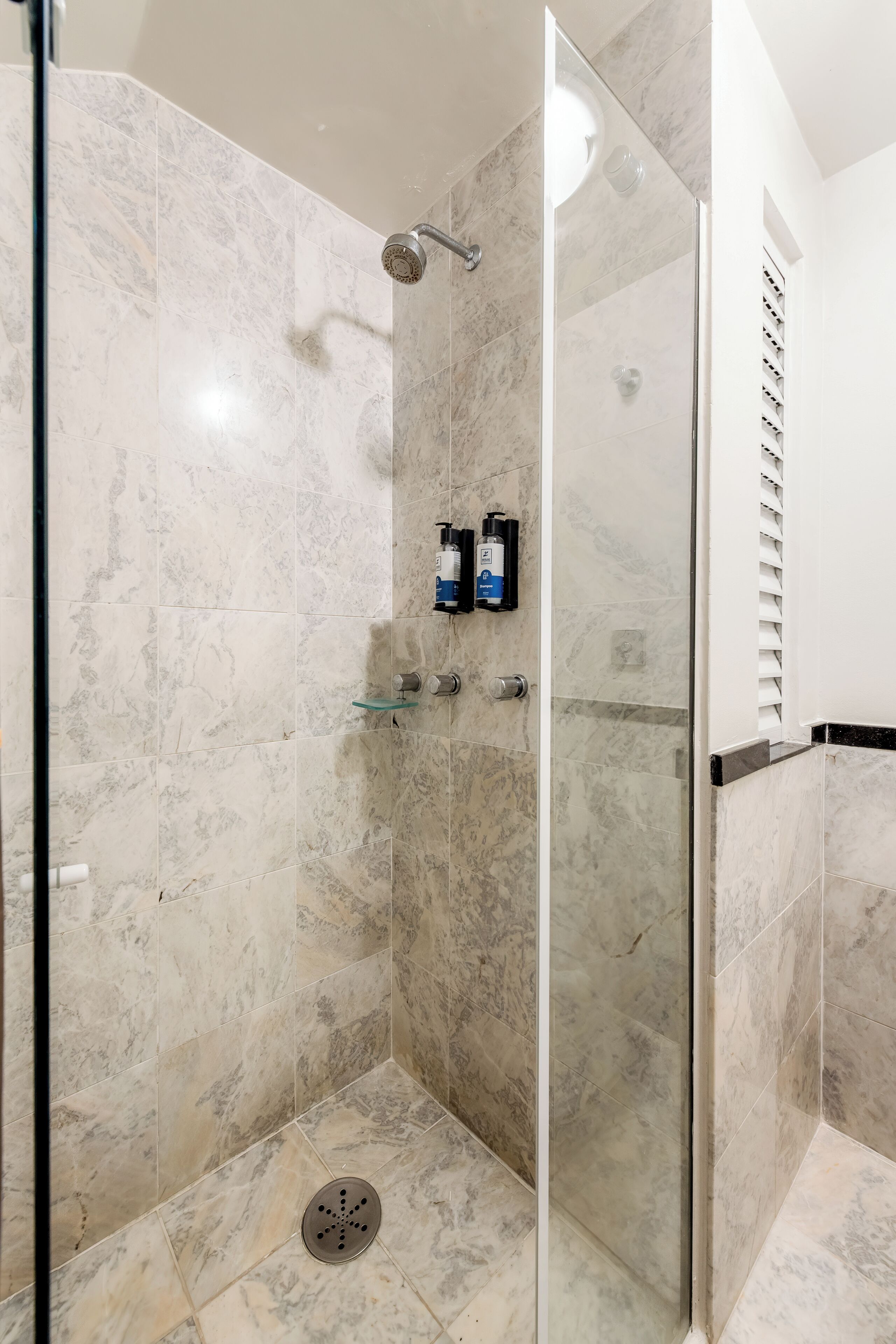 Un espace douche moderne avec des carreaux de marbre, une porte en verre et une petite étagère pour les articles de toilette.